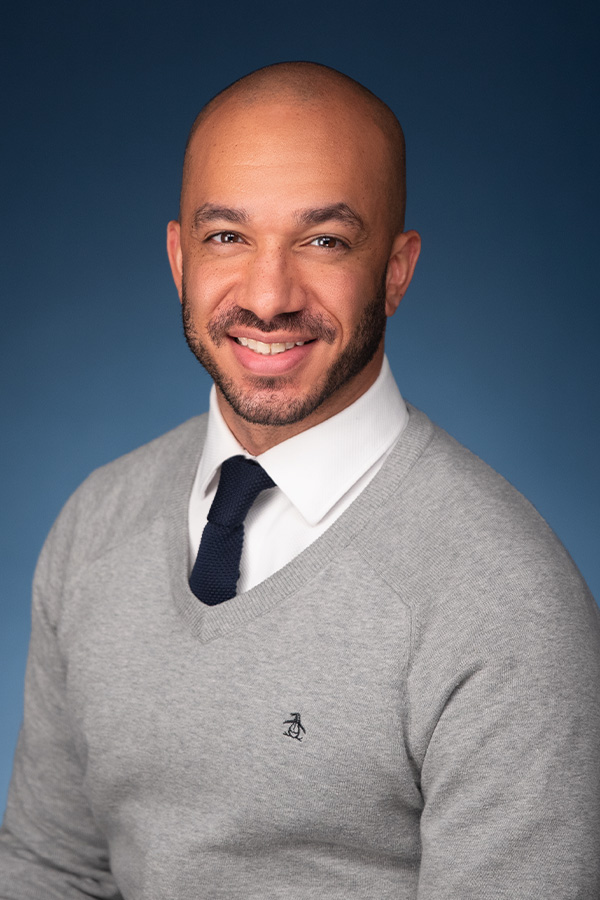 Headshot of Gaby, a Latina woman with short curly brown hair wearing a black hoodie and matching double earrings.