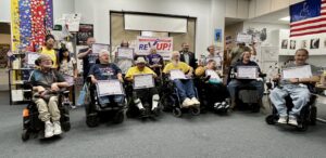 A group of REV UP coalition members, some of whom are in wheelchairs and others are standing in the back. All are holding signs. Bob is in the middle and front