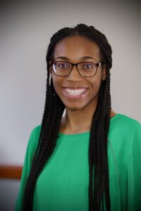 feoma is a Black woman with medium-dark complexion and long braids. She is wearing a green shirt. 