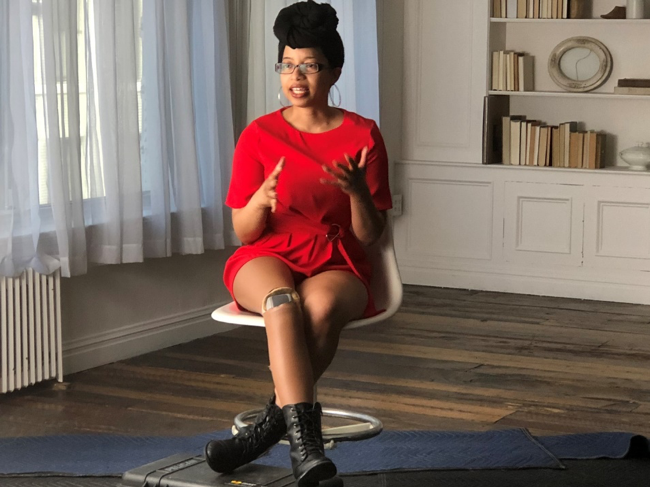 Photo of Keri Gray seated wearing a red dress and black boots